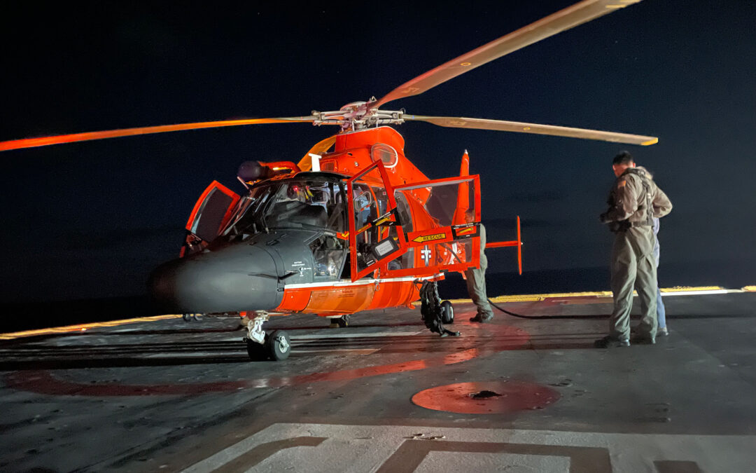 Coast Guard helicopter on a platform in the dark with a person standing next to it