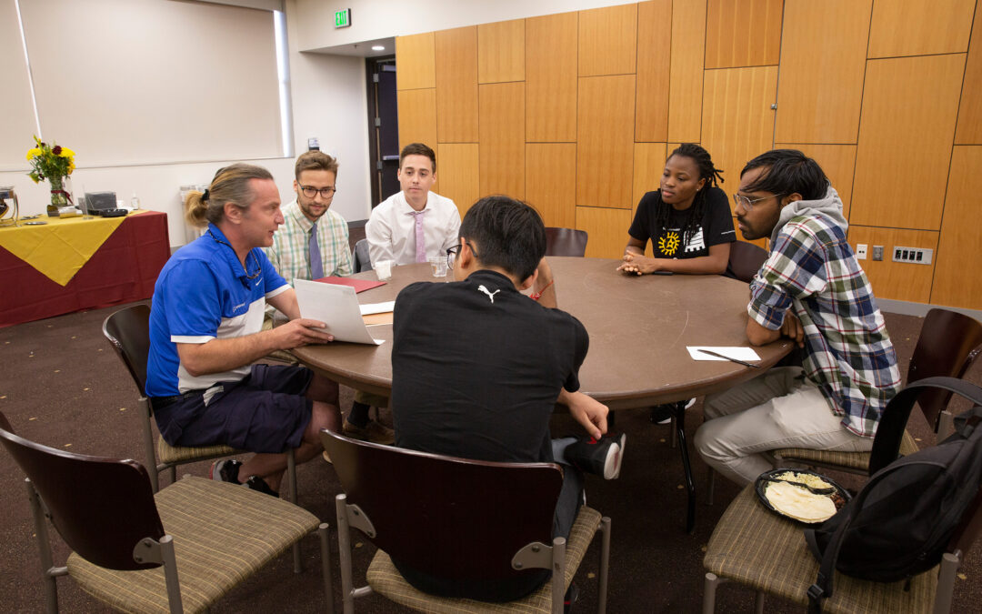 A group of students learns about career options from an engineer while sitting around a table
