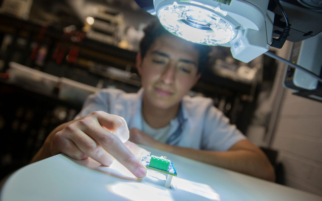 A student researcher works on electronic components in a lab.
