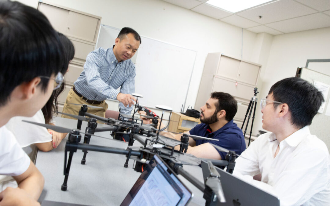 Yanchao Zhang talking to students in his lab around a table with a drone on it