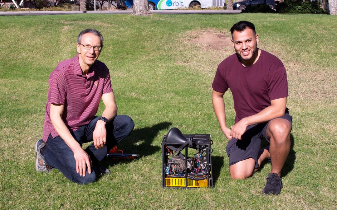 Two men stand with a battery power station powered by bicycle pedals in between them