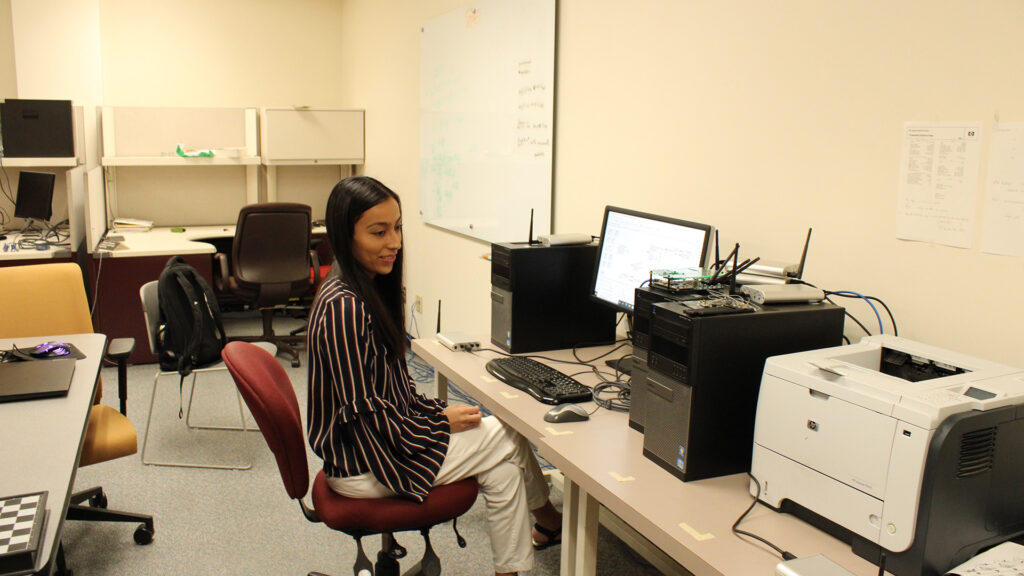 A woman looks at a printer and other electrical devices hooked to a computer for an experiment