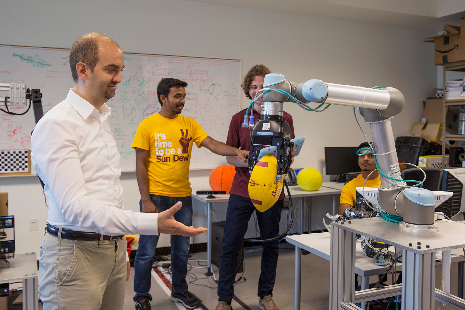 A robot grips a football as a faculty member and two students observe it