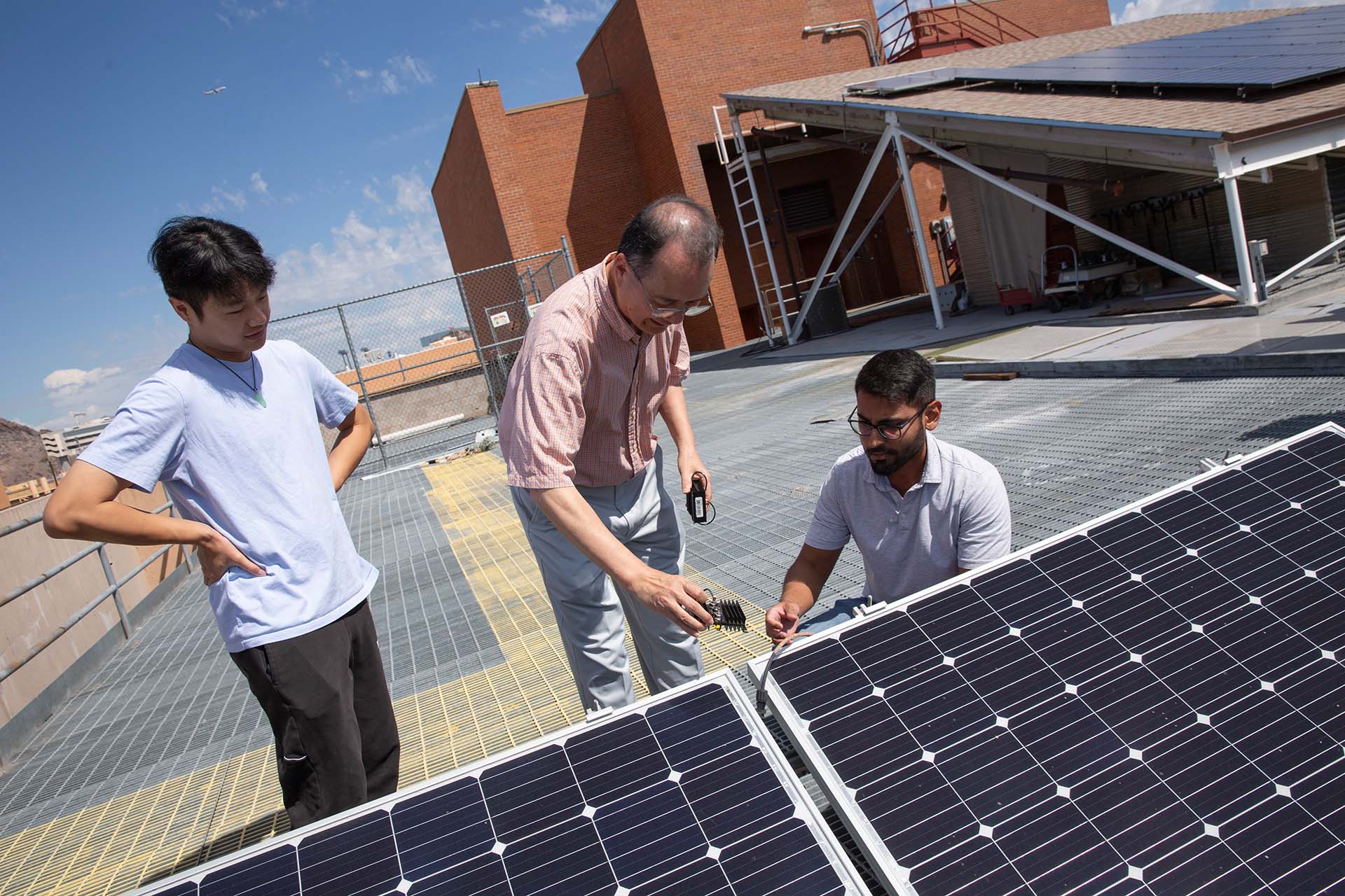 A faculty member works on solar technology on a rooftop with two students