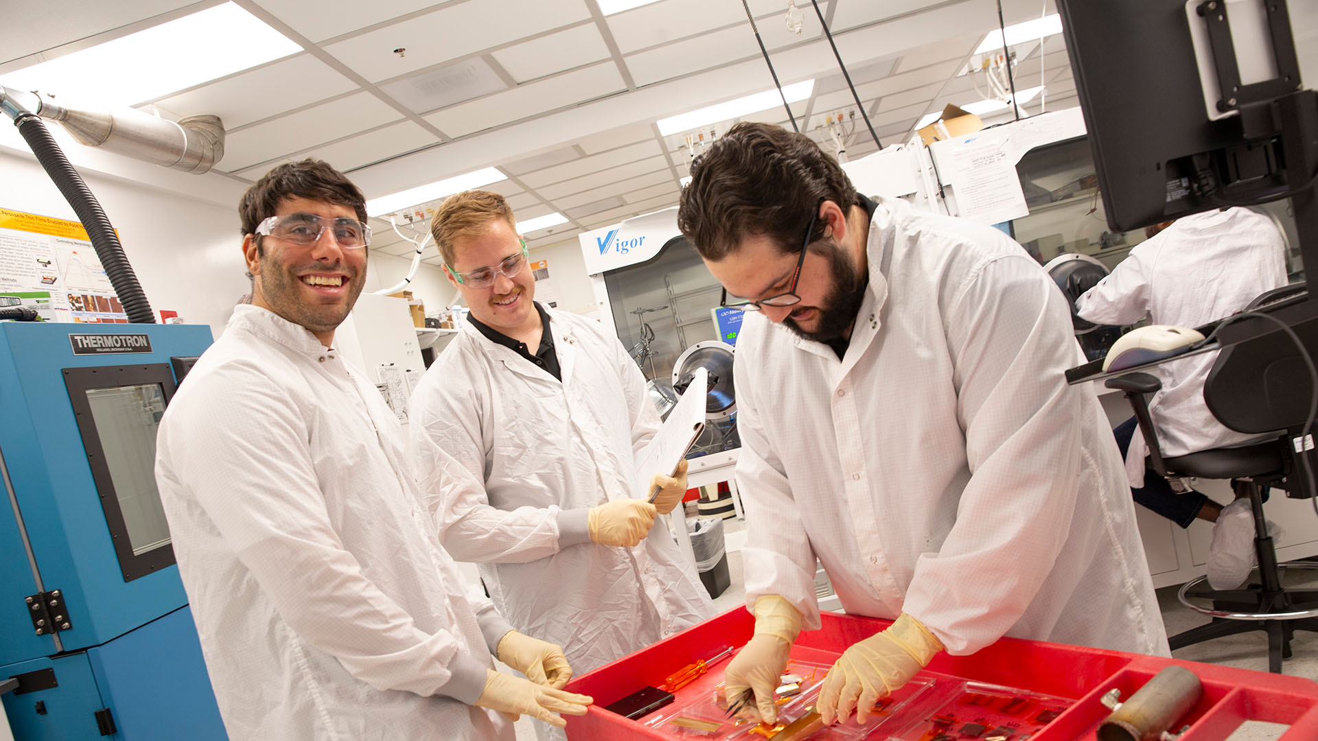 Faculty member works with two students in a lab on electrical equipment