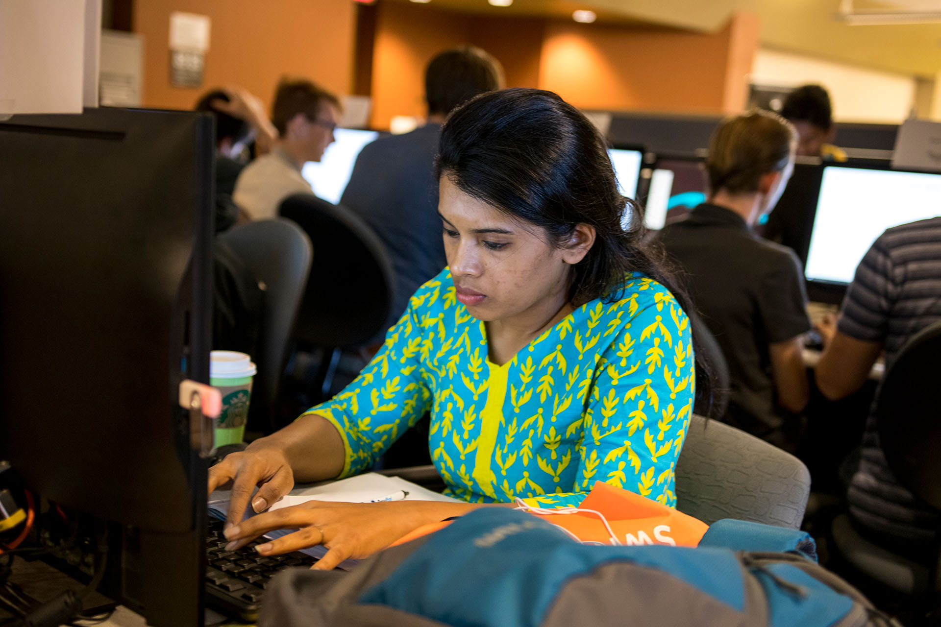 A woman types on a laptop in a room of people on computers