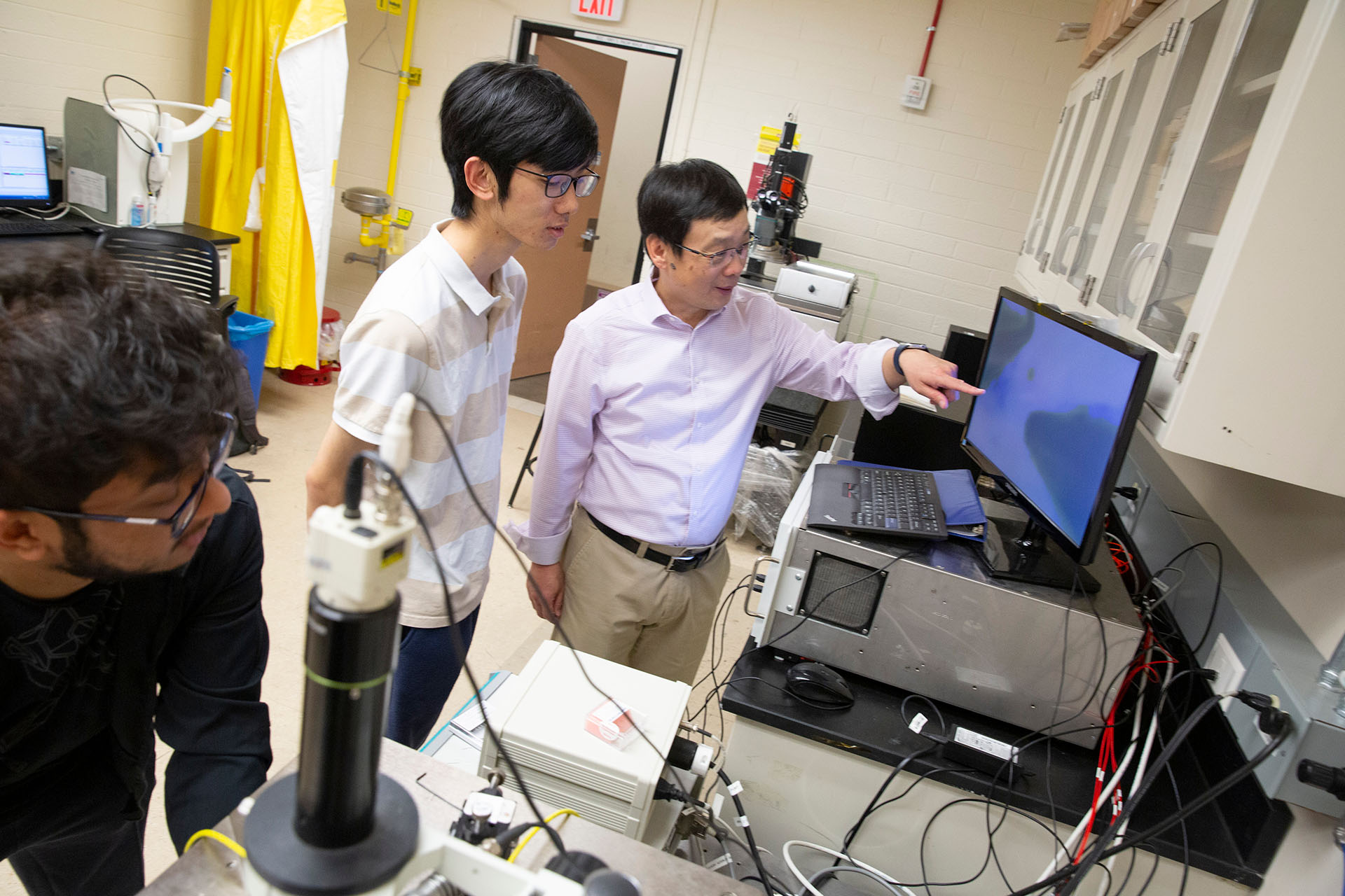 A man points at a computer screen while two others look on in a lab