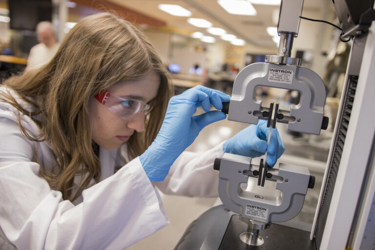 A student in a lab coat working on her project in a research lab.