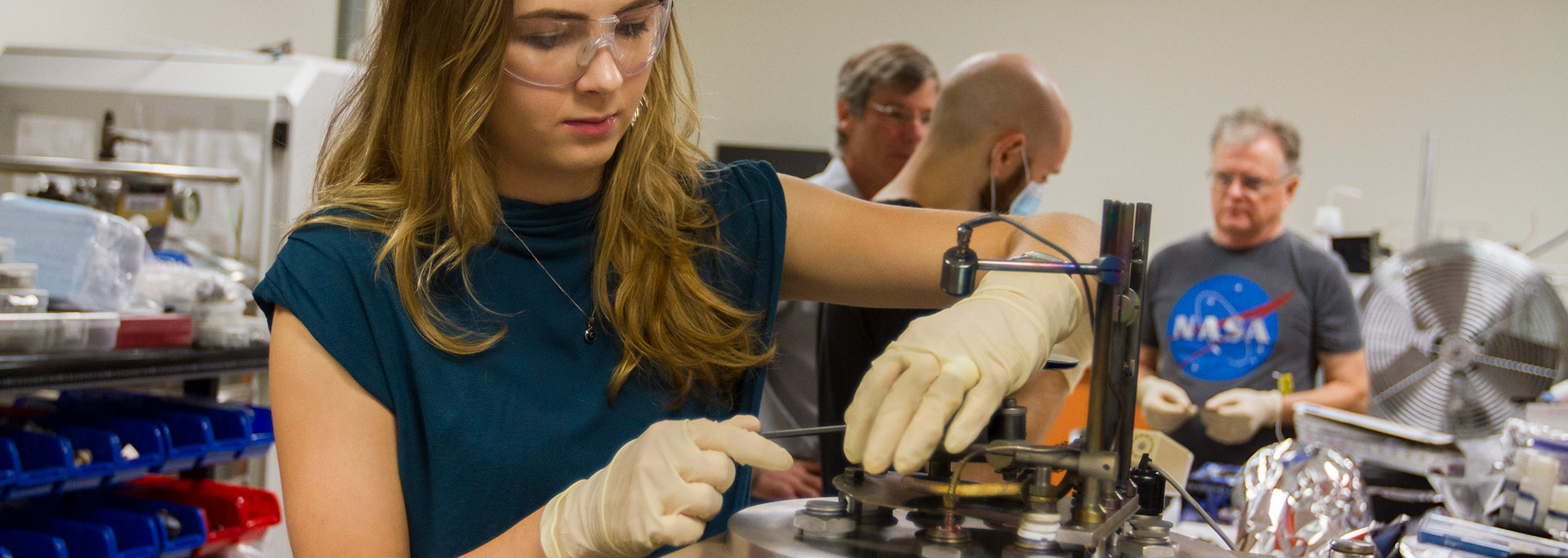 Female student wearing safety glasses building something in a lab.